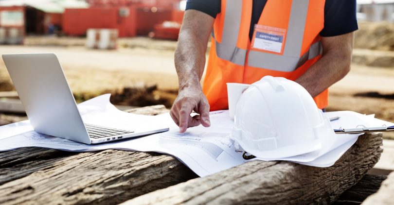 Closeup of contractor in construction site pointing at plan on wooden sleeper