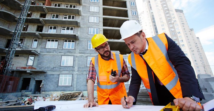 Modern engineer pointing at sketch in blueprint while explaining it to colleague